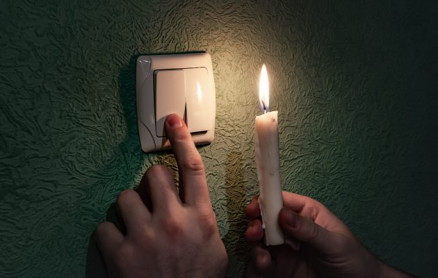 Holding burning candle in a dark room near a light switch, blackout. Power outage, energy crisis. Problems with power supply. Ukraine without power Holding burning candle in a dark room near a light switch, blackout. Power outage, energy crisis. Problems with power supply. Ukraine without power
